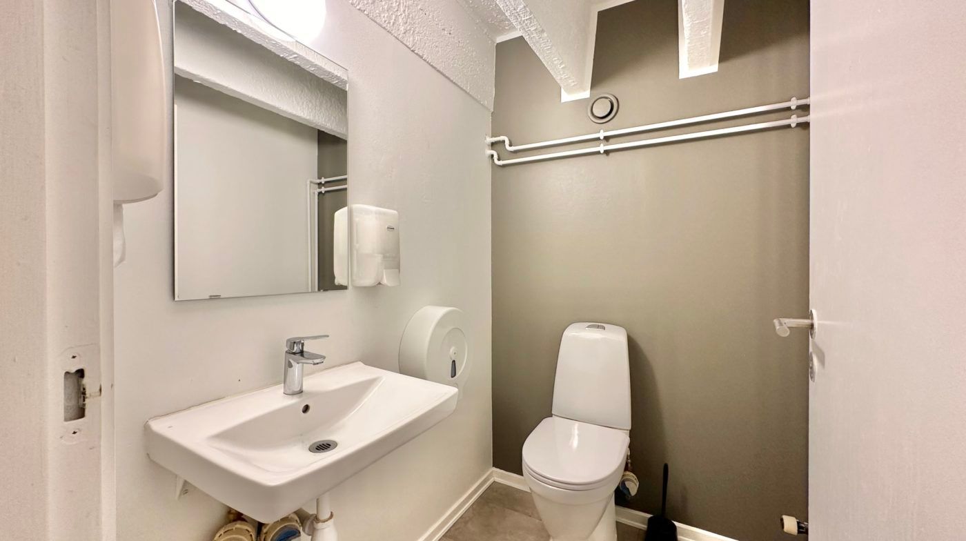 En lille ren toiletrum med en toilet, et håndvask, og en håndklædeautomat.