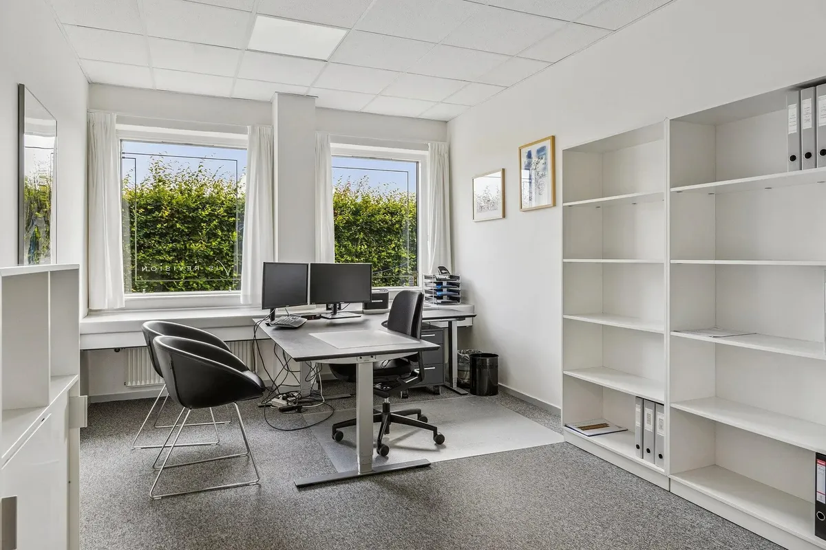 Kontorrum med skrivebord, to skærme, to stole, bibliotek og vindue med udsigt til haven udenfor