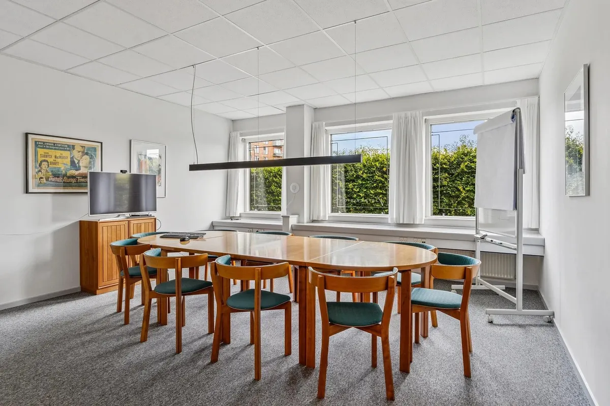 Kontorlokaler med langt borde og stole samt tv og skrivebord i et roligt miljø med højt beløb og udsigt til haven udenfor