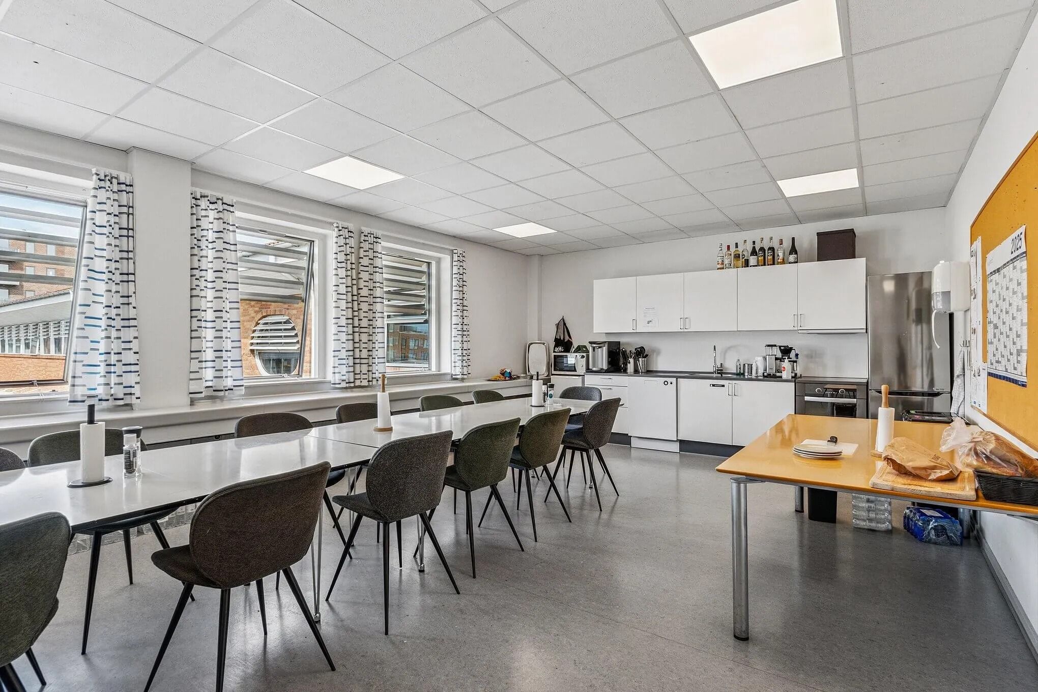 Kontorrum med lange lyse træborde og stole samt hvide loftsbelægninger og lysegule vægge