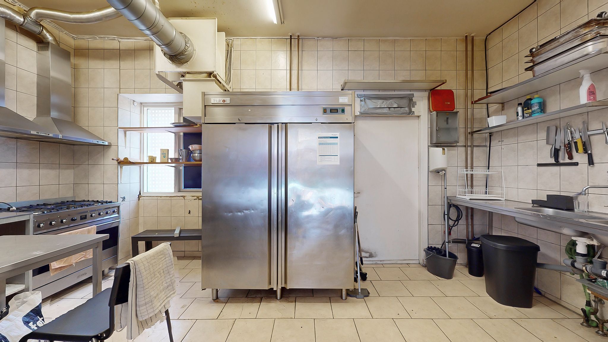 En køkken med flere apparater og husholdningsgenstande, herunder en stor køleskab og en ovn samt en rensningsstang og en