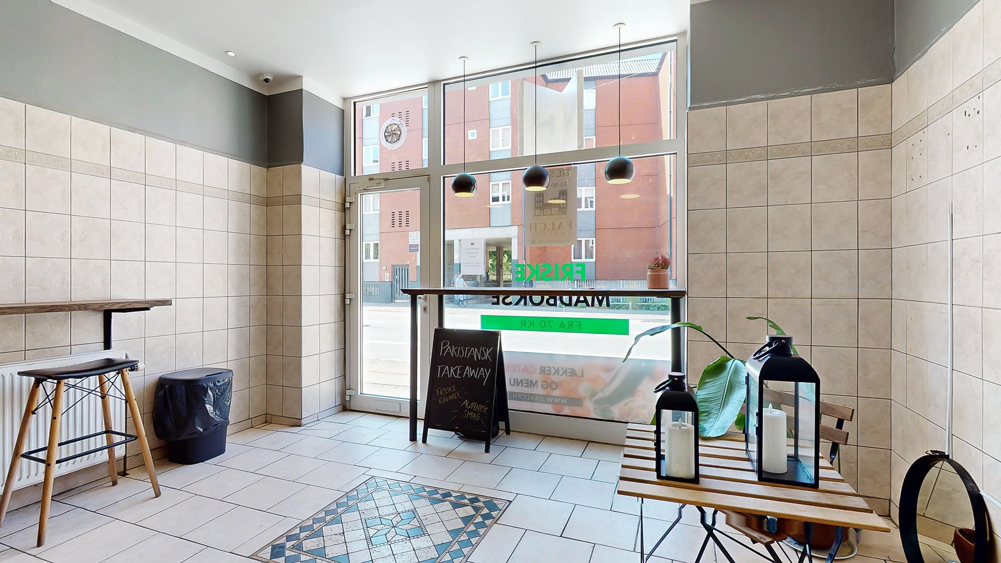 Erhvervslokale med vinduer og tagetage, med et bord og en menu på en tavle, og en plante i en lanterne