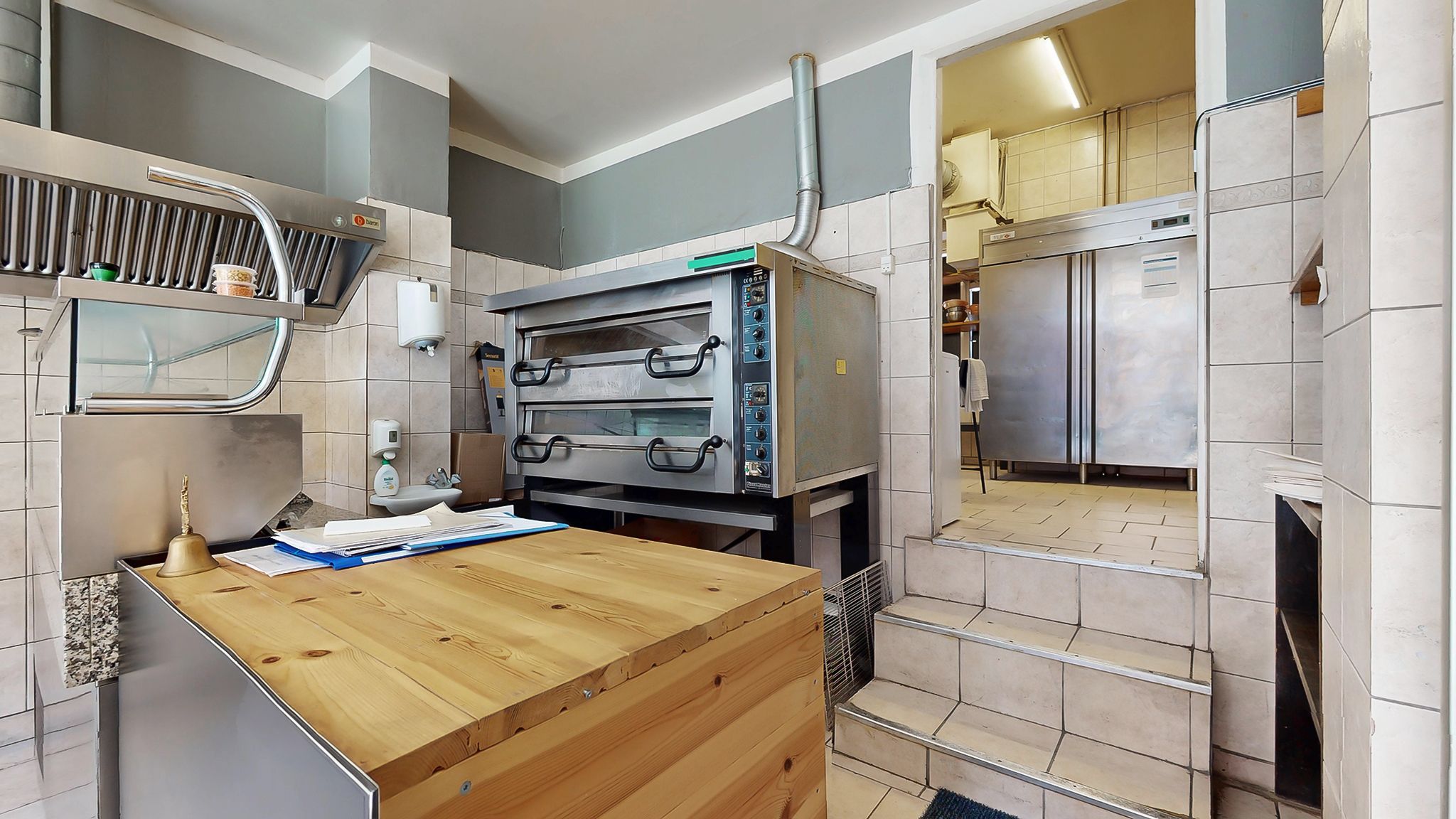 En kombineret køkken og bageri med en stor ovn og et træbord med papirer og en bjælke på bordet