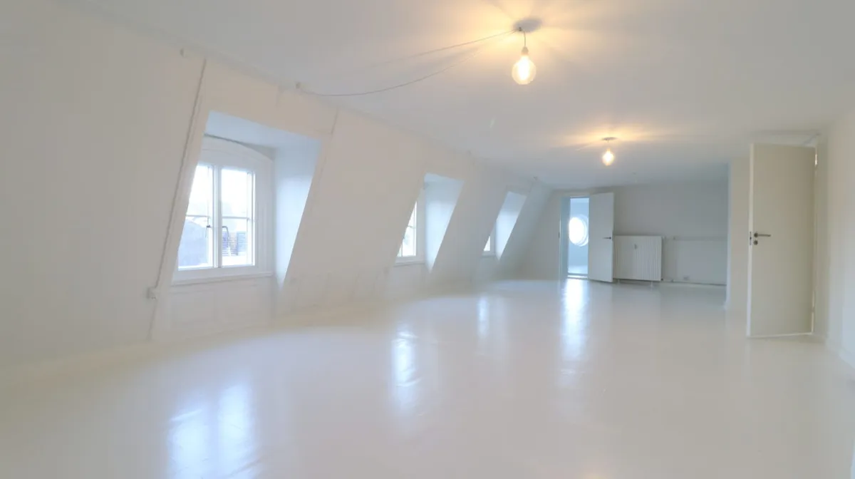 Et stort lyse og rent loftsrum med hvide vægge og gulve og flere store vinduer