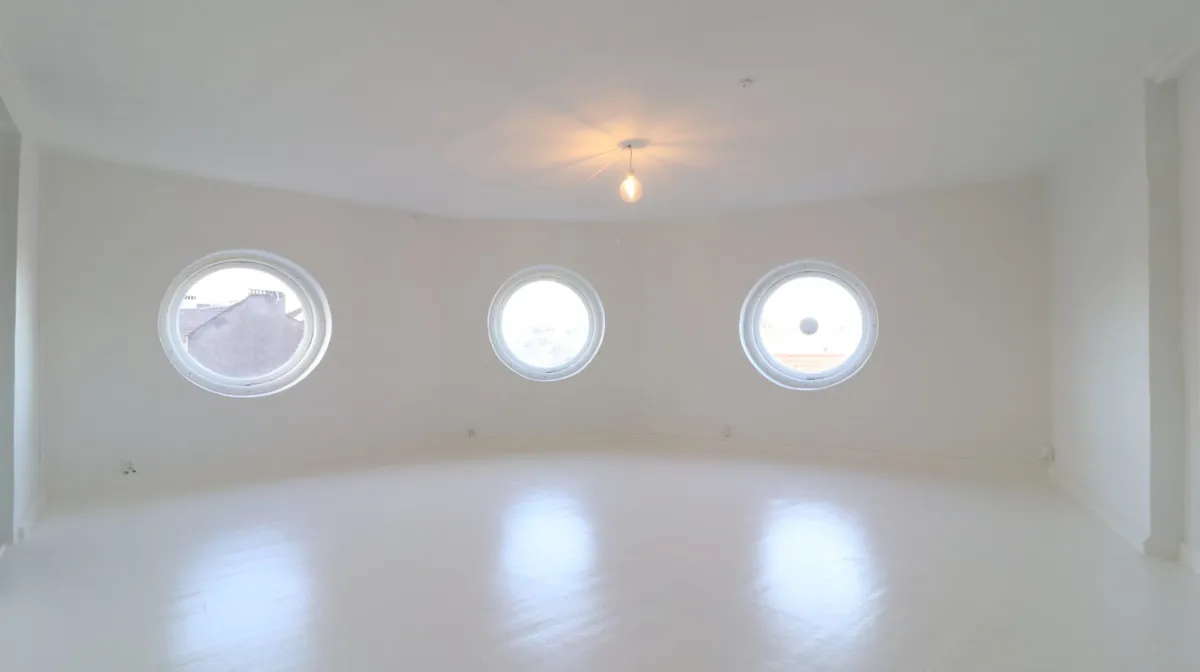 En rektangulær kontorlokal med hvide vægge, loft og gulv samt tre runde vinduer med hvide omrammer