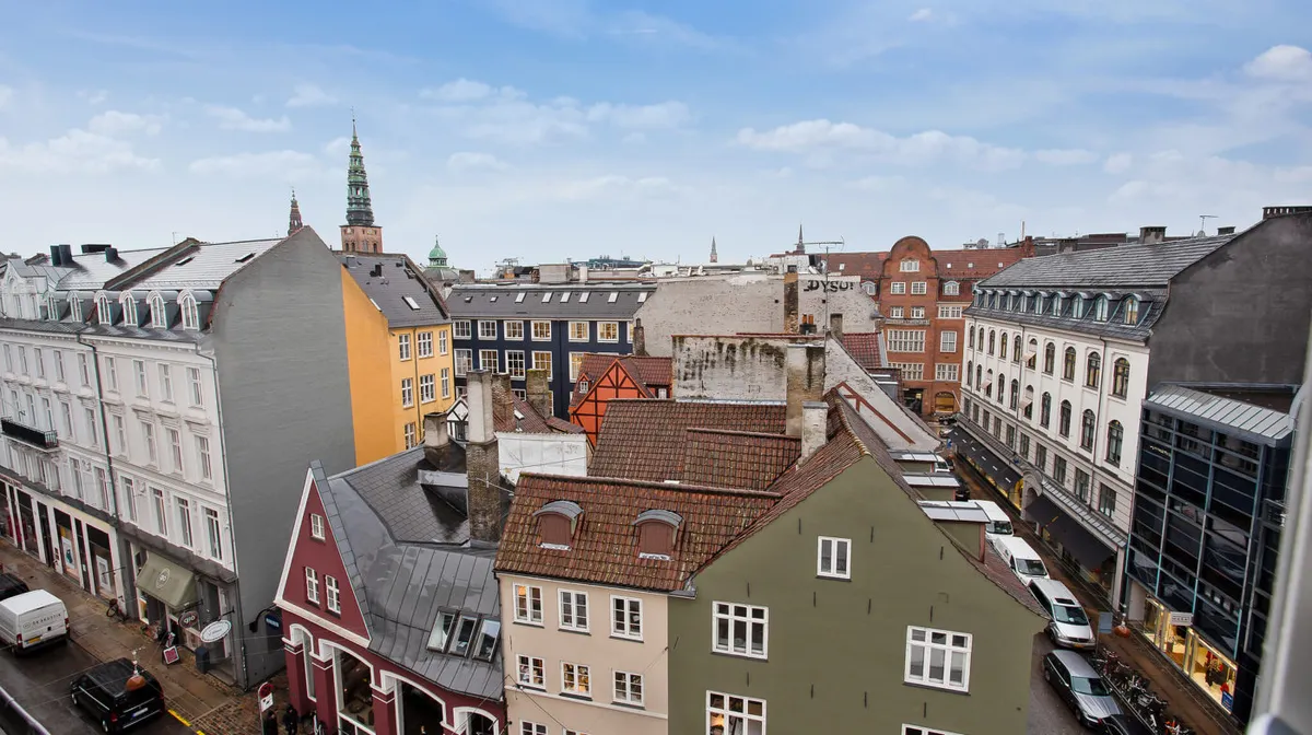 Farverige bygninger med huse i forskellige farver og stilarter, og adskillige biler og lastbiler parkeret i gaden