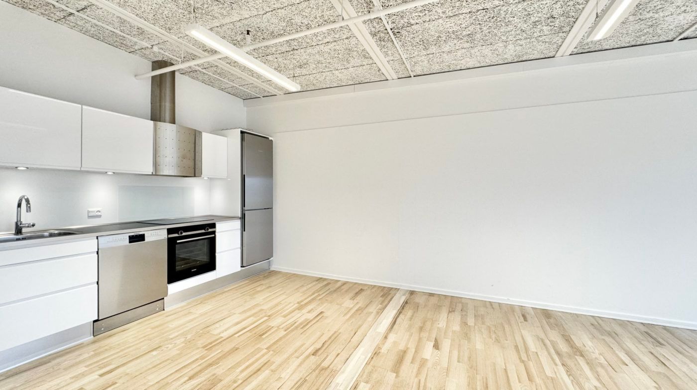 En moderne køkken med hvide vægge, brædder og højloft samt lyse loftslampe. Et komfur, ovn og en køleskab er installeret.