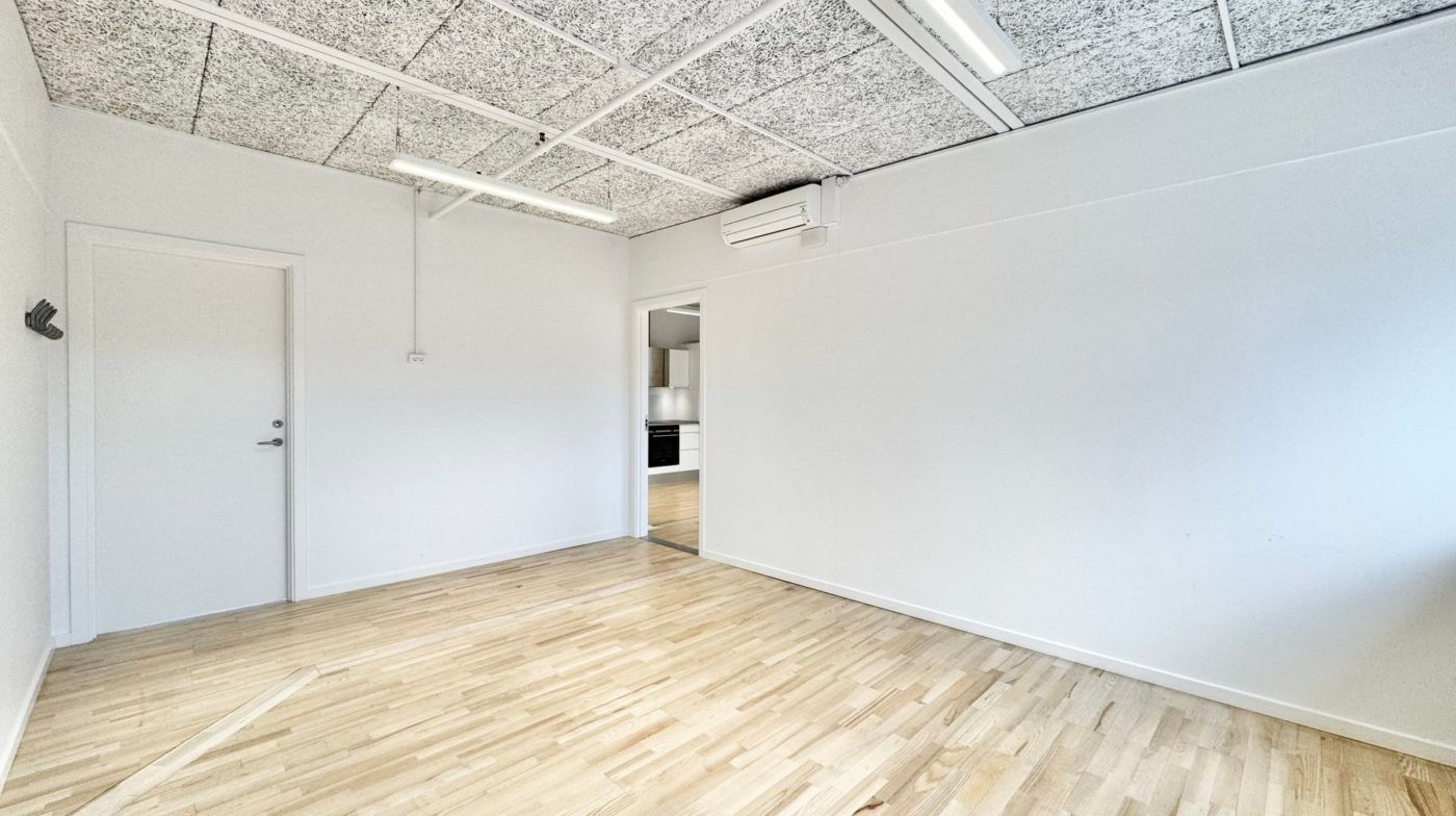 Kontorlokaler med lyse hvide vægge og lofter, hvor trægulvet reflekterer lyset og skaber en moderne og reneste atmosfære