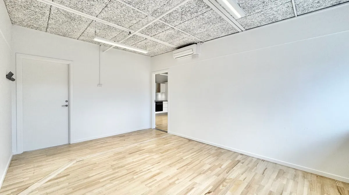 Kontorlokaler med lyse hvide vægge og lofter, hvor trægulvet reflekterer lyset og skaber en moderne og reneste atmosfære