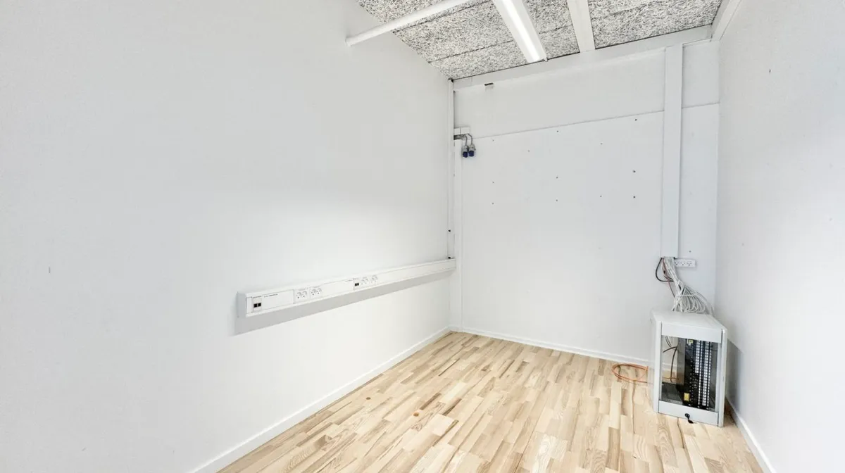 Rum med hvidt loft og hvidt vægpanel samt trægulv og elektriske stikkontakter og ledningsforløb på væggen