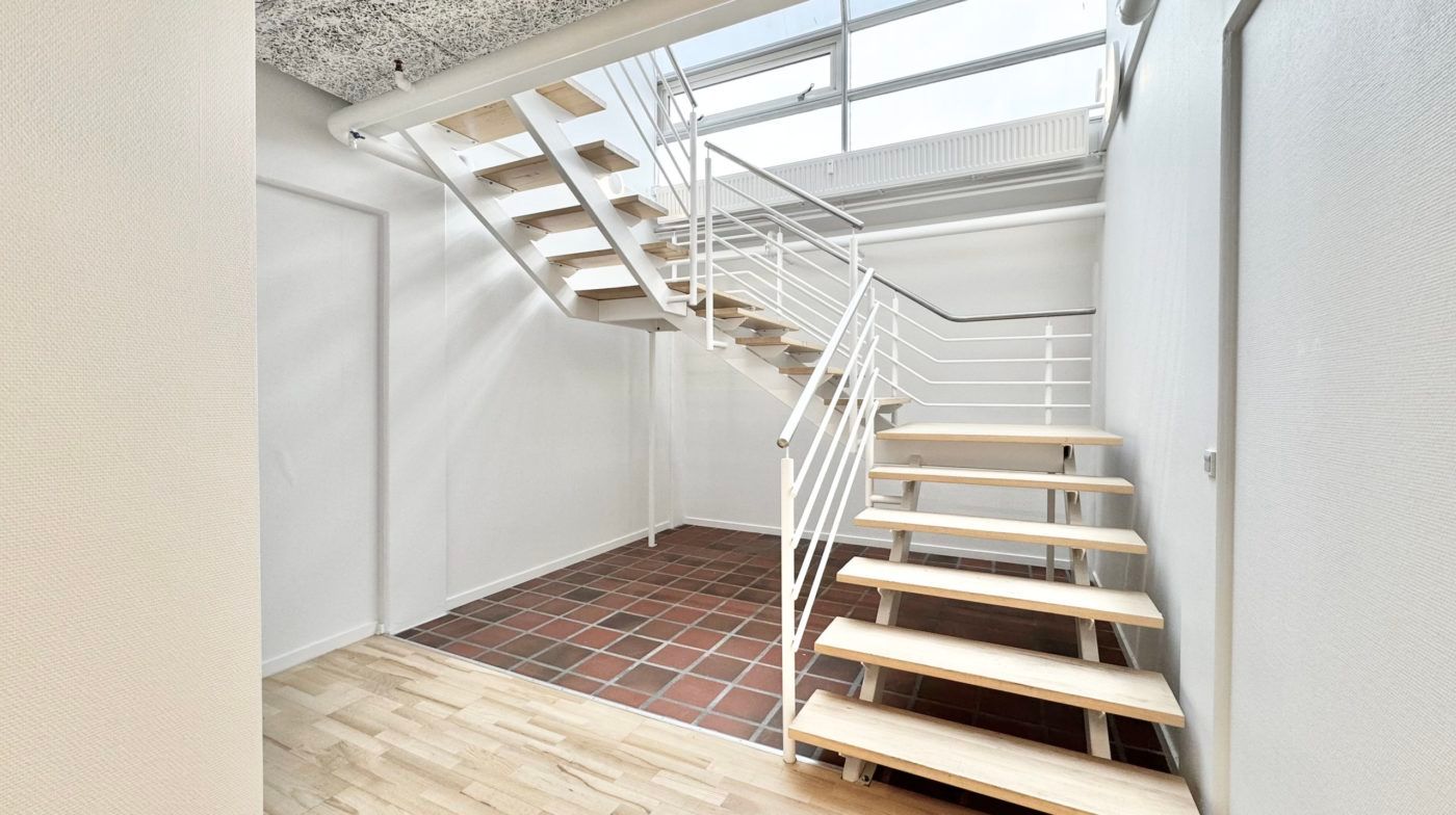 Hvidt trægulv og hvide vægge med lyseruder og trapper og håndtag i hvidt metal uden møbler og genstande