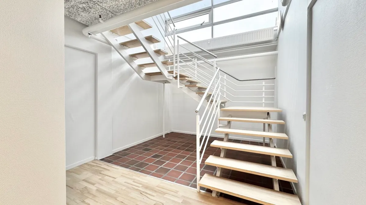 Hvidt trægulv og hvide vægge med lyseruder og trapper og håndtag i hvidt metal uden møbler og genstande