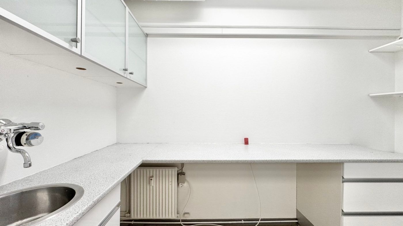 Moderne kontorlokaler med hvidt loft og vægge, en hvid bordplade, en hvid radiator og en hvid metalvaskedis med håndtryk og