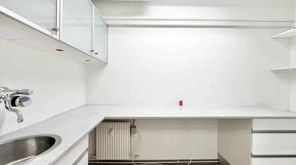 Moderne kontorlokaler med hvidt loft og vægge, en hvid bordplade, en hvid radiator og en hvid metalvaskedis med håndtryk og