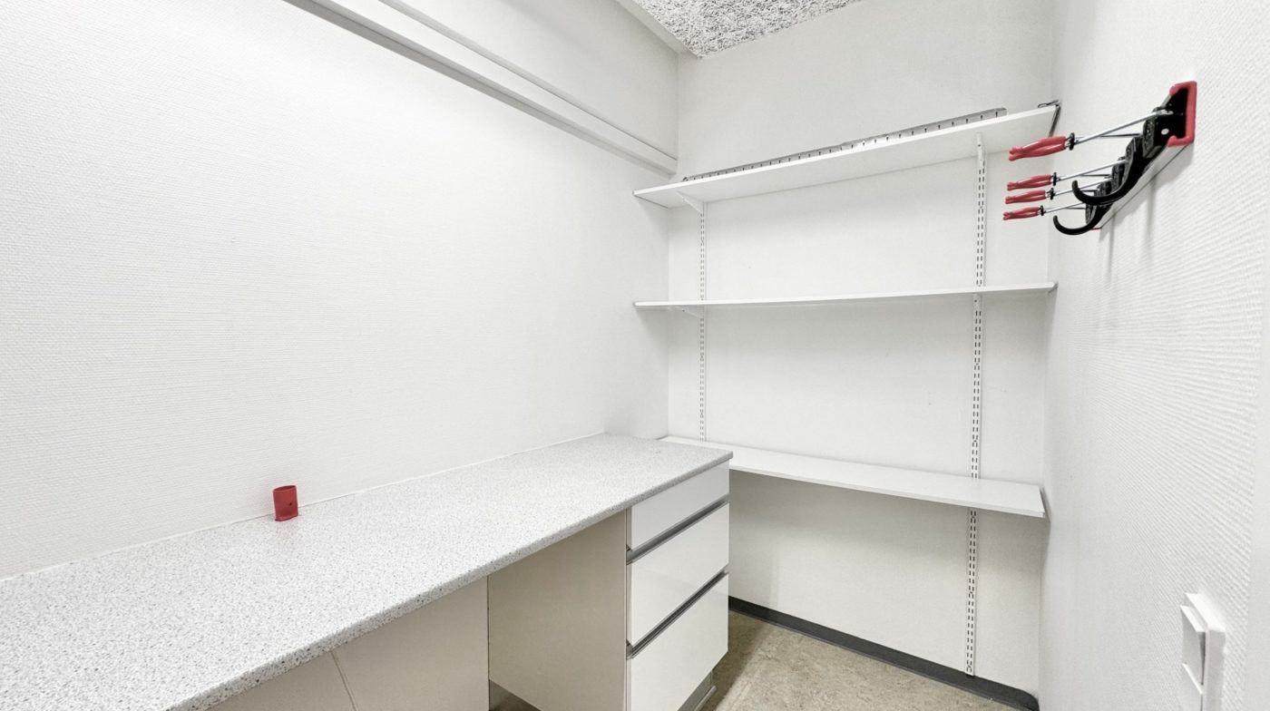 Kontorlokaler med to høje hylder og en hvid skrivebord. Skrivebordet har tre høje sektioner og er lavet af marmor. Væggene