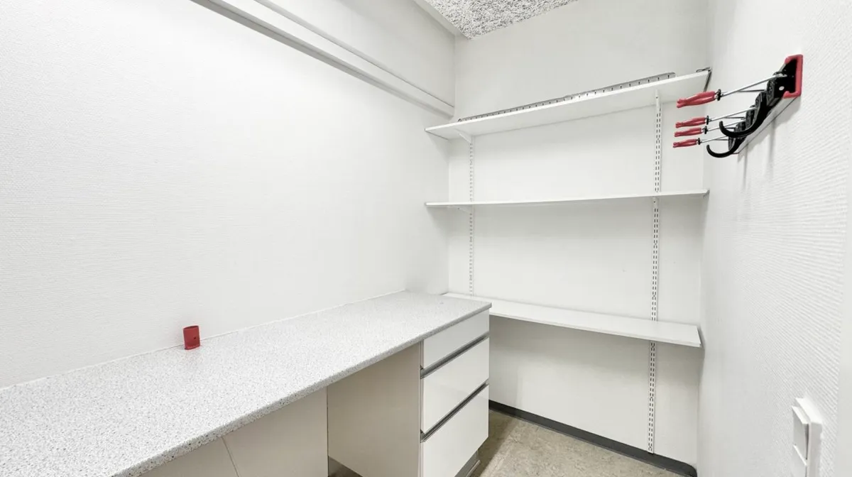 Kontorlokaler med to høje hylder og en hvid skrivebord. Skrivebordet har tre høje sektioner og er lavet af marmor. Væggene