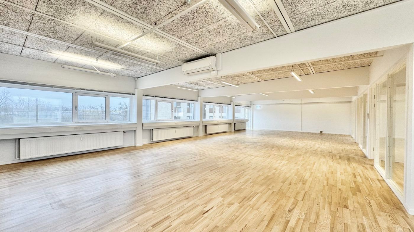 En stor, tom kontorbygning med hvide vægge og lysegult trægulv, samt flere store vinduer og moderne klimaanlæg