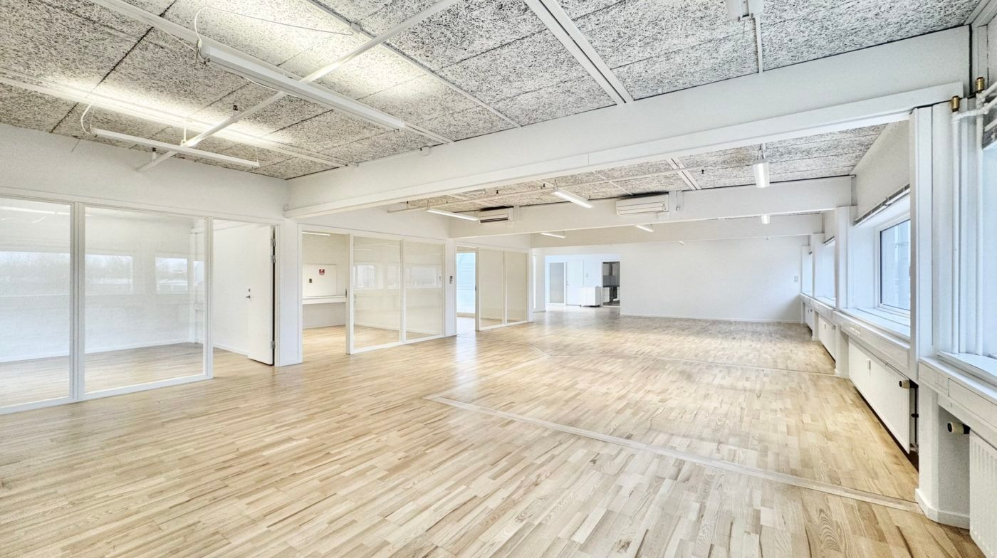 Et stort, tomt kontor med hvidt loft og hvide vægge, hvor gulvet er lavet af træ og vinduer med glaspartier og hvide rammer