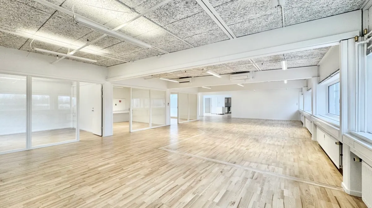 Et stort, tomt kontor med hvidt loft og hvide vægge, hvor gulvet er lavet af træ og vinduer med glaspartier og hvide rammer