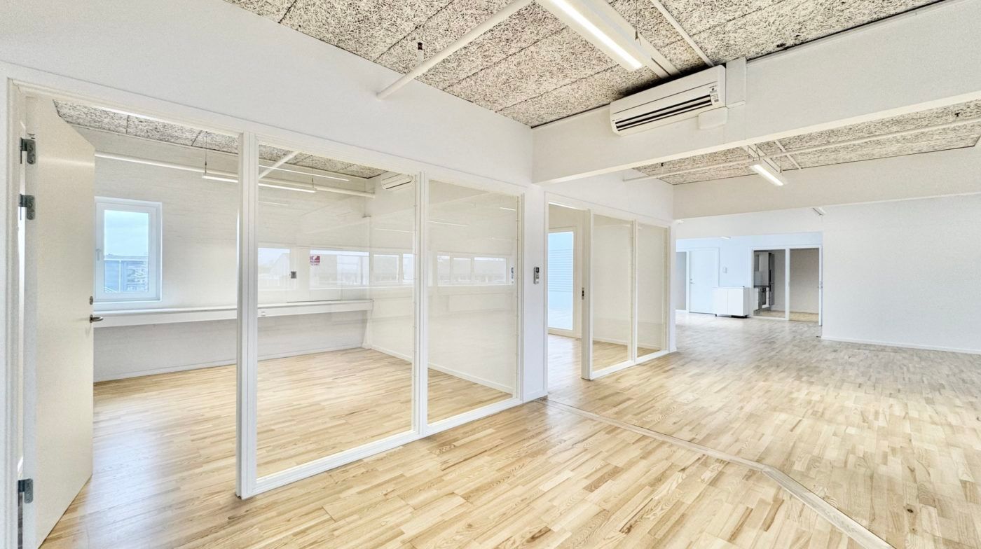 Kontorlokaler med hvide vægge og glasdøre samt trægulve og klimaanlæg i loftet. Lokalerne er lyse og velorganiserede med