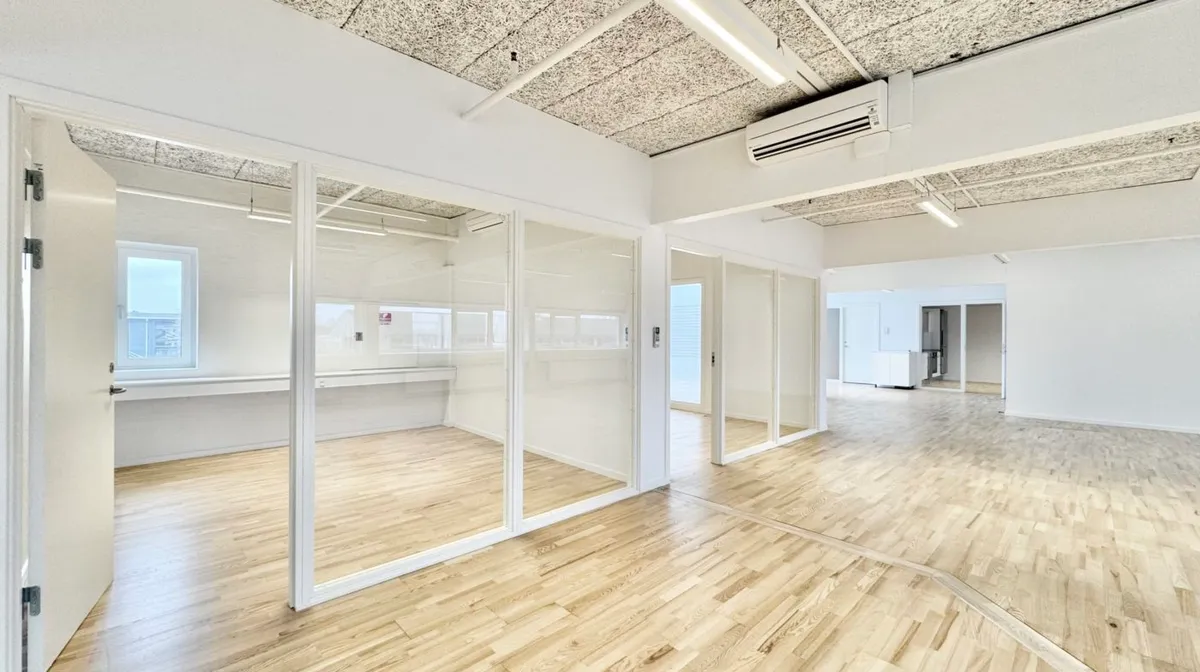 Kontorlokaler med hvide vægge og glasdøre samt trægulve og klimaanlæg i loftet. Lokalerne er lyse og velorganiserede med