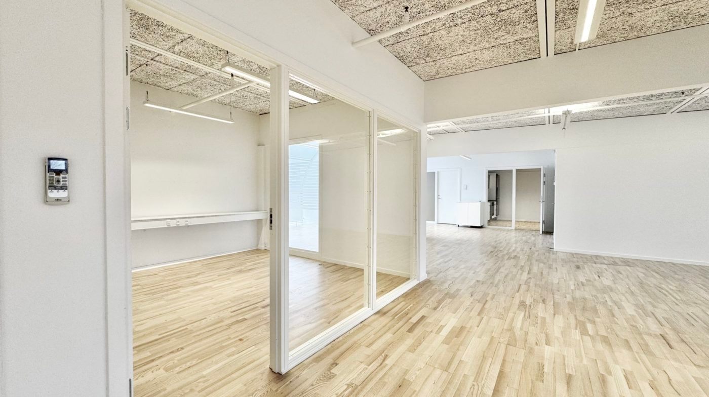 Elegant og åben kontor med lyse trægulve og hvide vægge samt store glasdøre og klimaanlæg i højre side