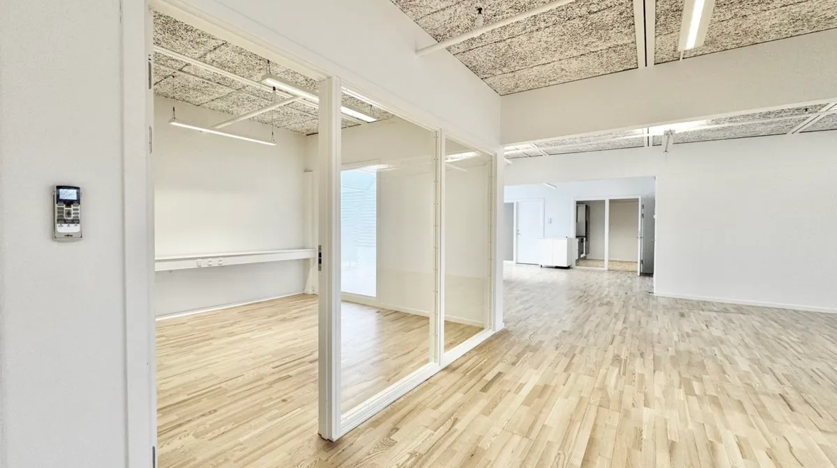 Elegant og åben kontor med lyse trægulve og hvide vægge samt store glasdøre og klimaanlæg i højre side