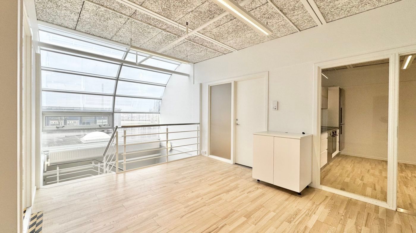 Minimalistisk indretning med højloft og lyseruder samt en stor balkon med udsigt til gaden og bygninger