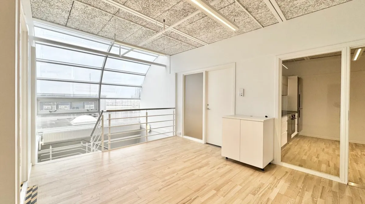 Minimalistisk indretning med højloft og lyseruder samt en stor balkon med udsigt til gaden og bygninger