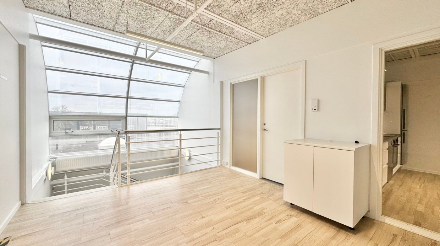 Moderne kontor med glasvinduer og højloft i hvidt. Trægulv og lyse tage med stålhåndtag på altan. Væggene er hvide med en