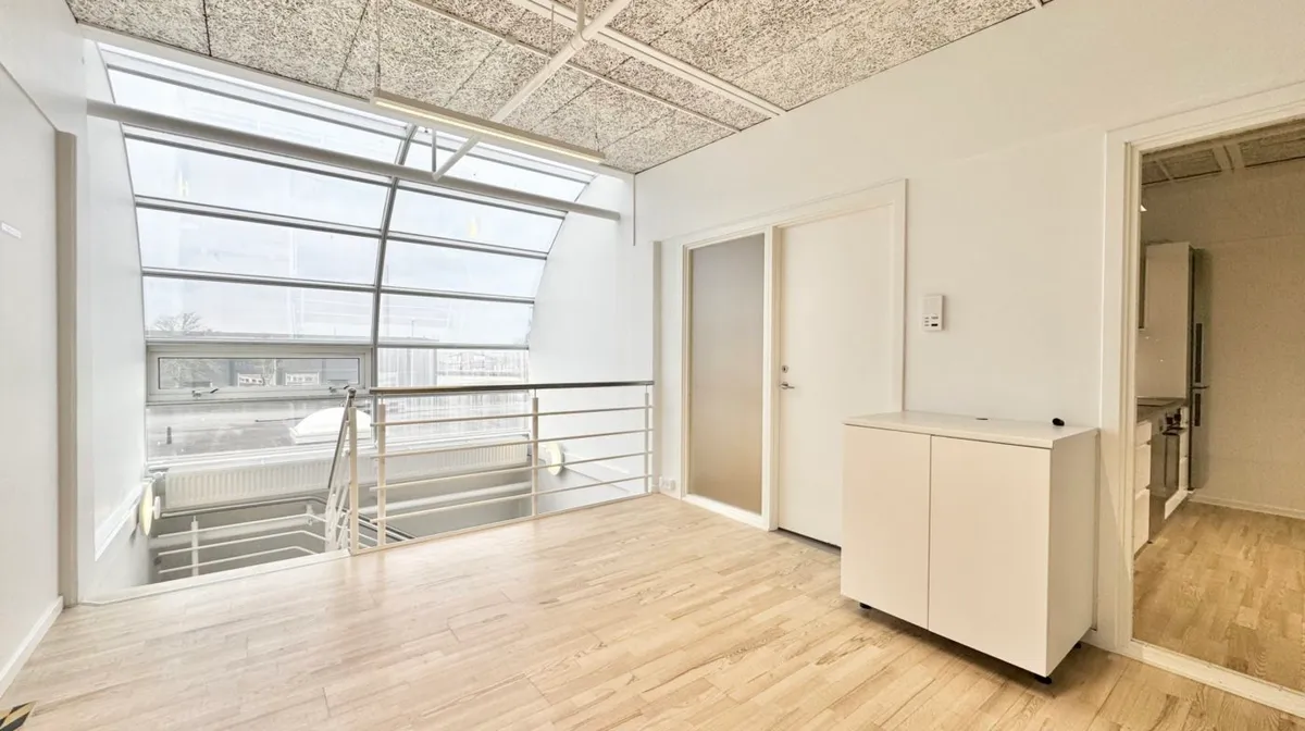 Moderne kontor med glasvinduer og højloft i hvidt. Trægulv og lyse tage med stålhåndtag på altan. Væggene er hvide med en