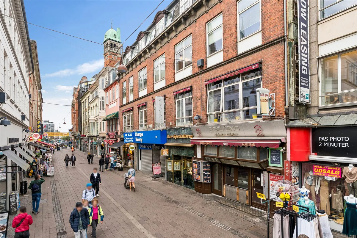 Mennesker går rundt på en butiksfyldt gågade, og butikkerne har skilte som Sam Bar Karaoke, Ray-Specialisten, Restaurant