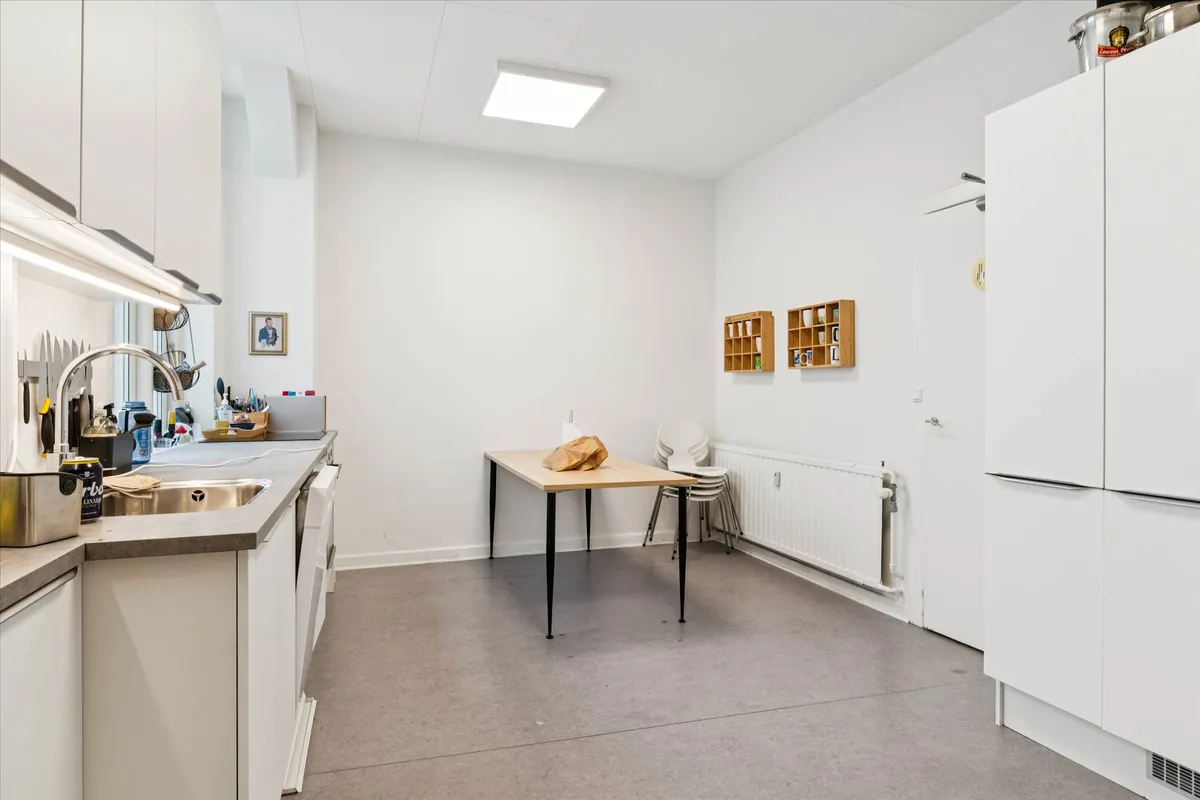 Lyst og rent køkken med hvide vægge, lysegul gulv og moderne møbler samt en ovn og køleskab