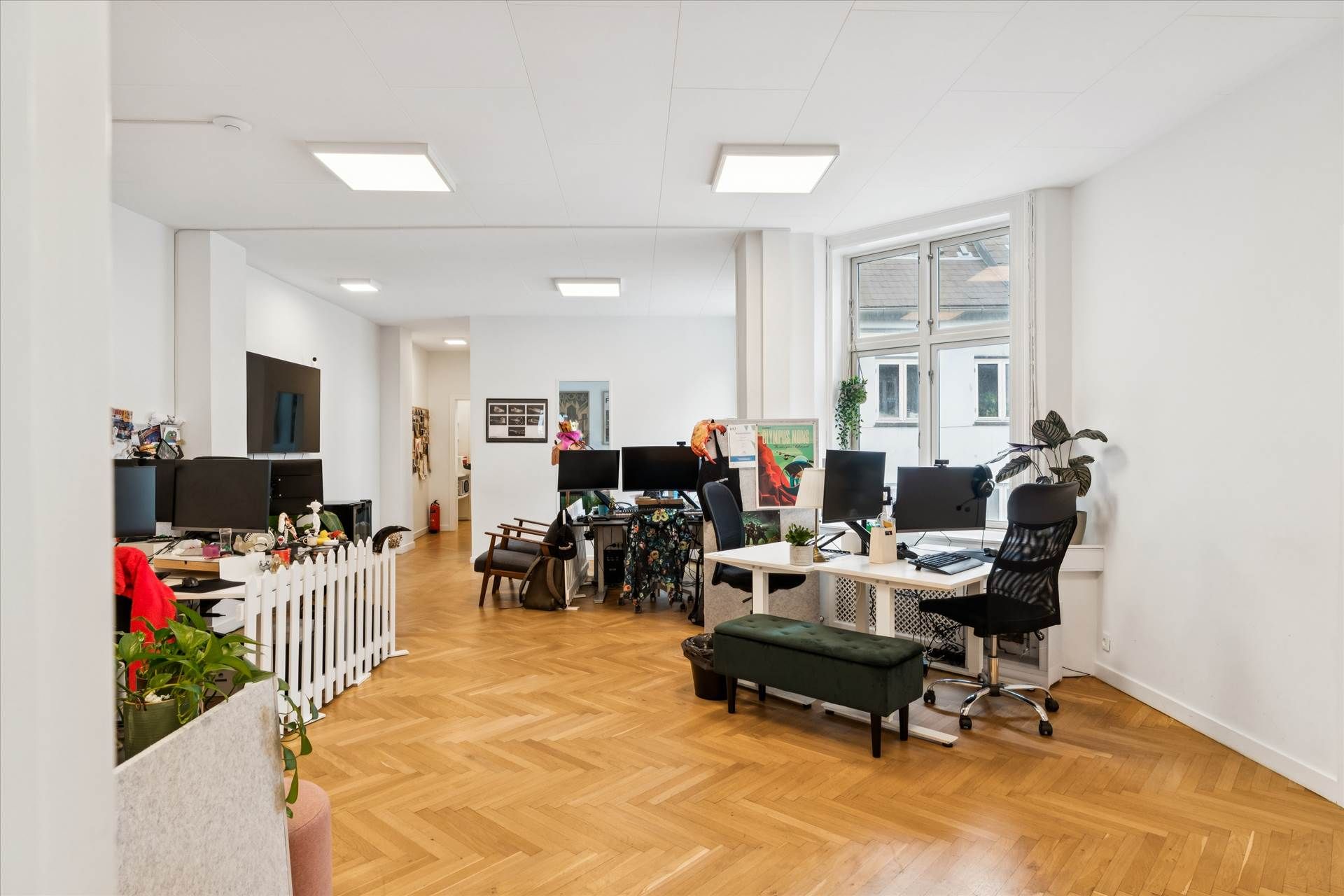 Et moderne og lyst kontor med højloftede rum, hvidt panel og trægulv, computere og skriveborde, og dekorationer på væggene