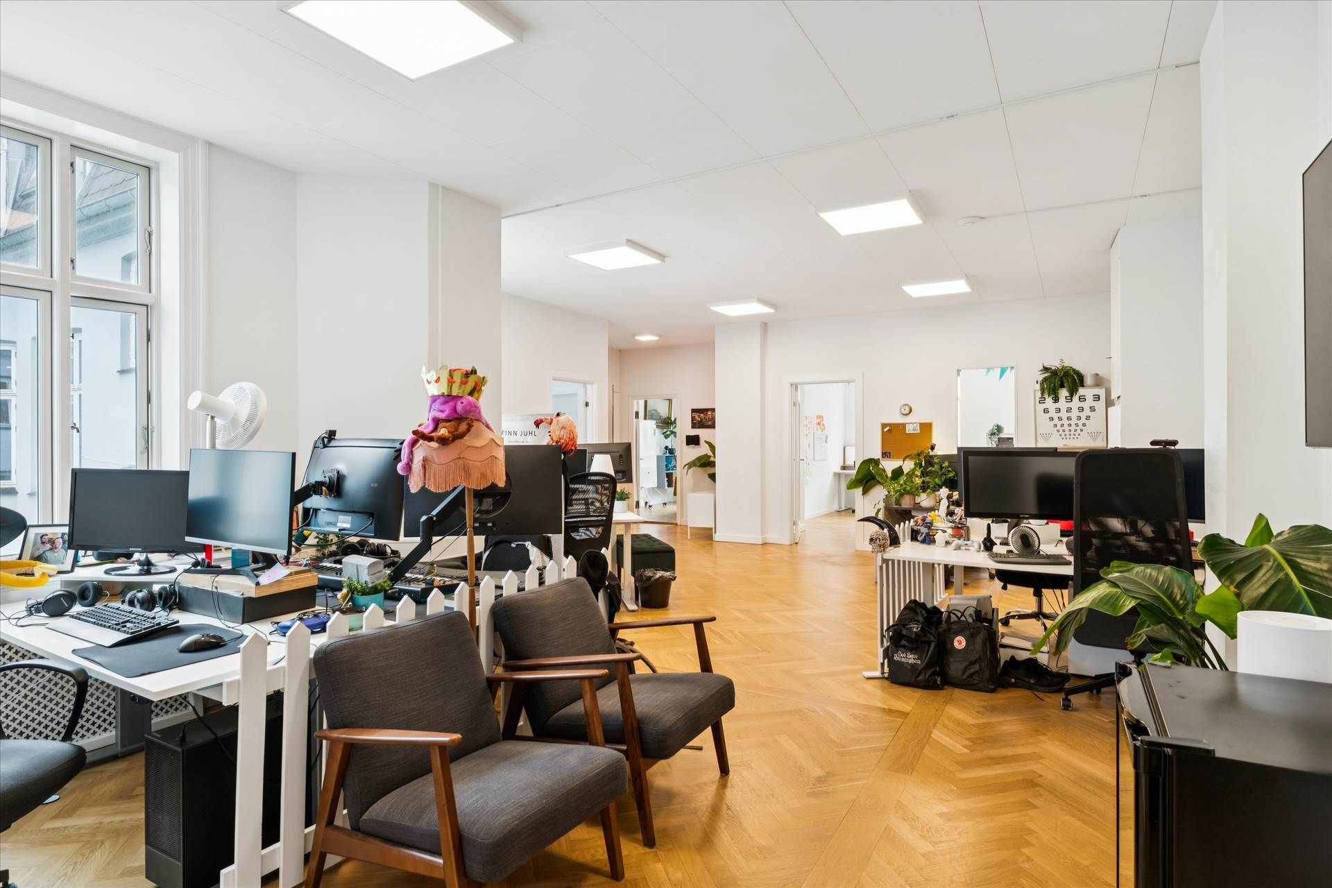 Lyst kontor med moderne møbler og højloftede værelser, fuld af skriveborde, stole, plantepoteter og computere samt et køkken