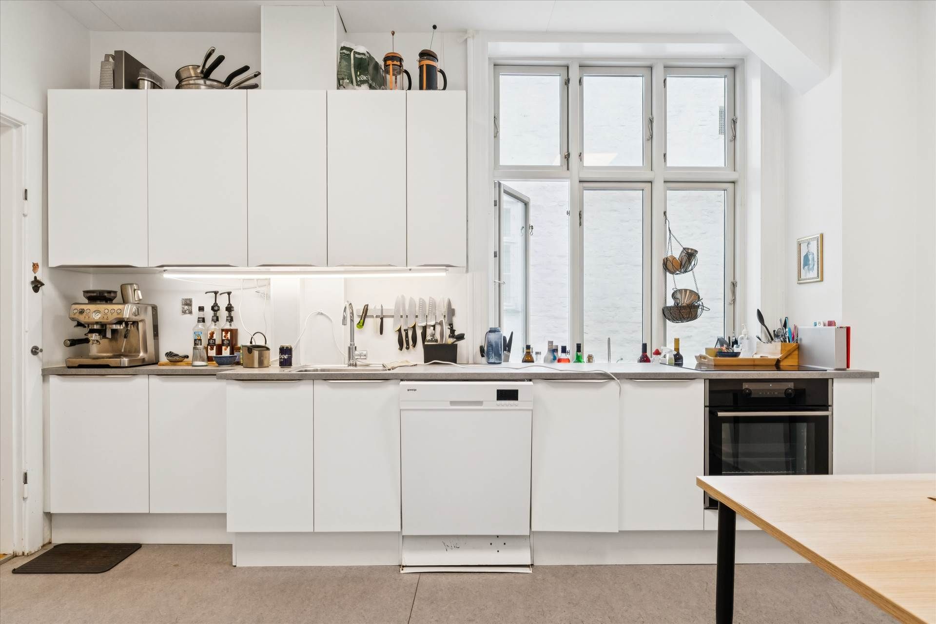 En moderne hvid køkken med en række apparater og kogegrej samt en spisestue, der er placeret i en lyse og veludstyret