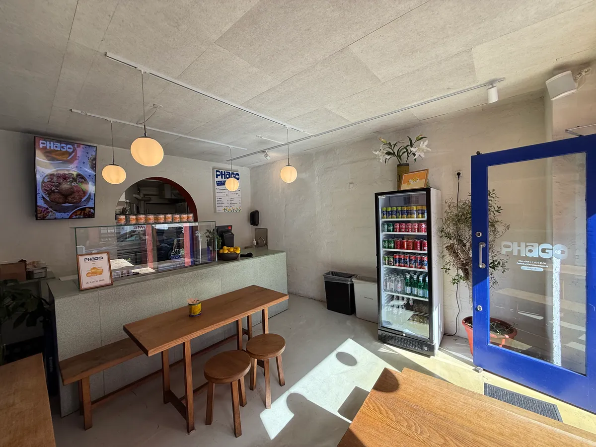 Take-away med køkken og salgssted i København N med moderne møbler og udstykning samt køleskab med drikkevarer