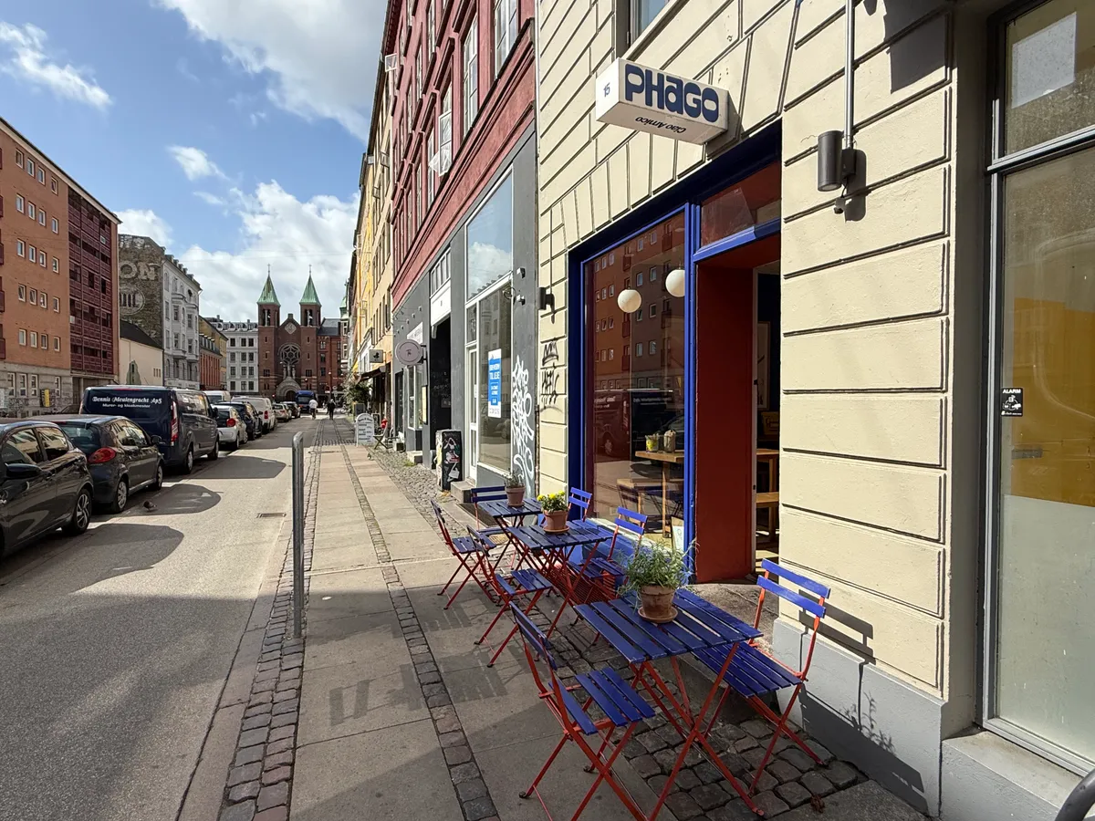 Take-away med røde stole og borde på gågaden med restauranten Phago i baggrunden