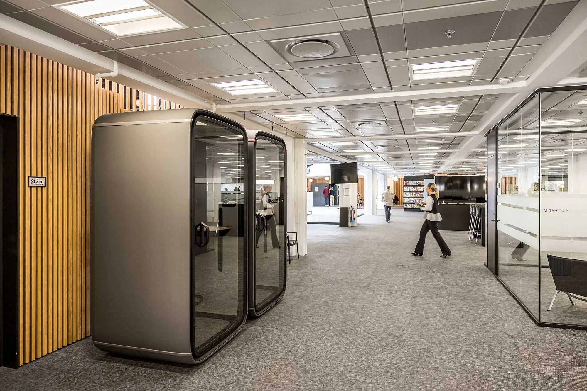 Kontorlokaler med moderne glasvægge og møbler og en person, der går i den anden ende af lokalet