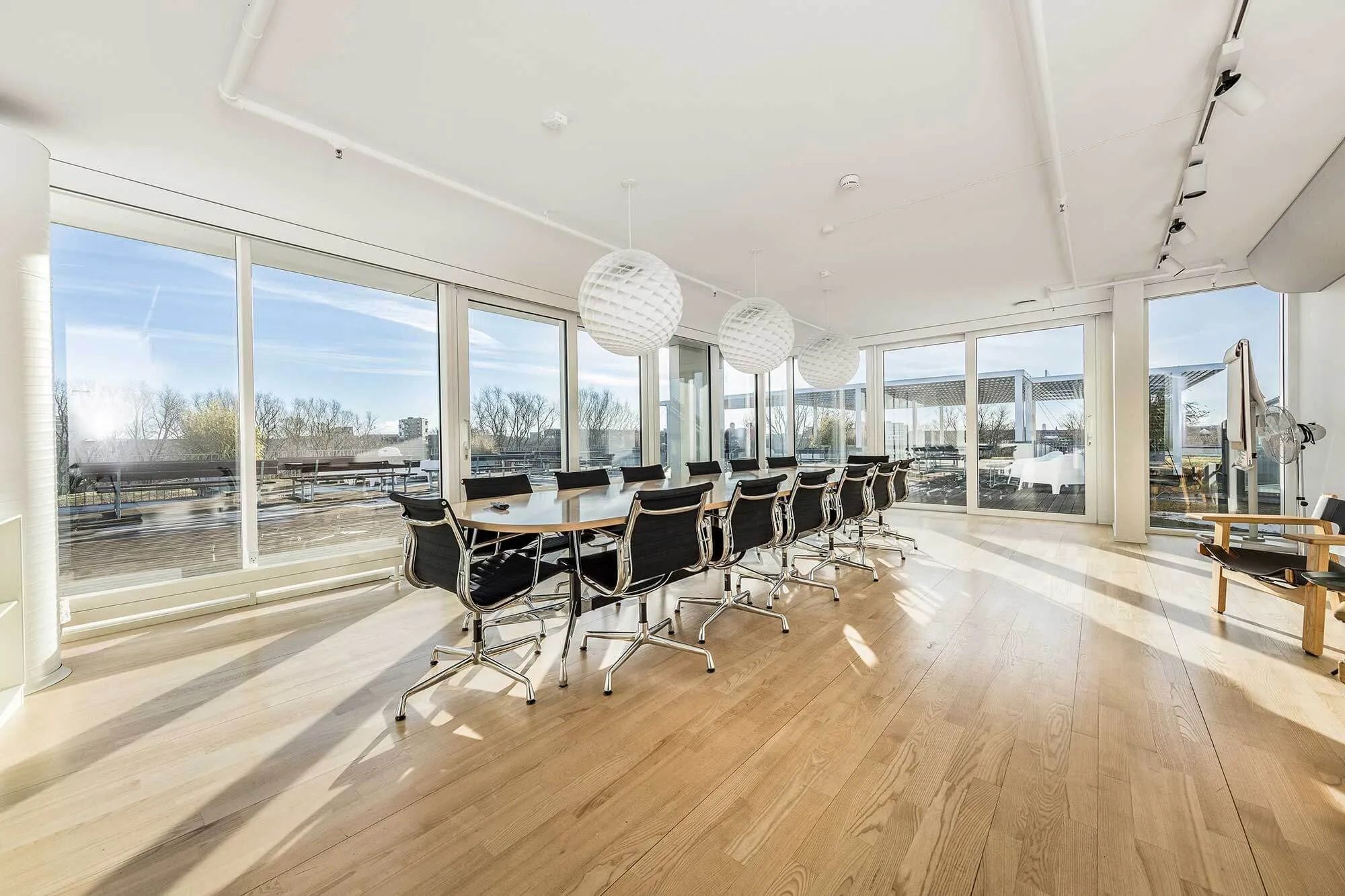 En mødehal med lyse trægulve, store vinduer og møbler i sort og hvid