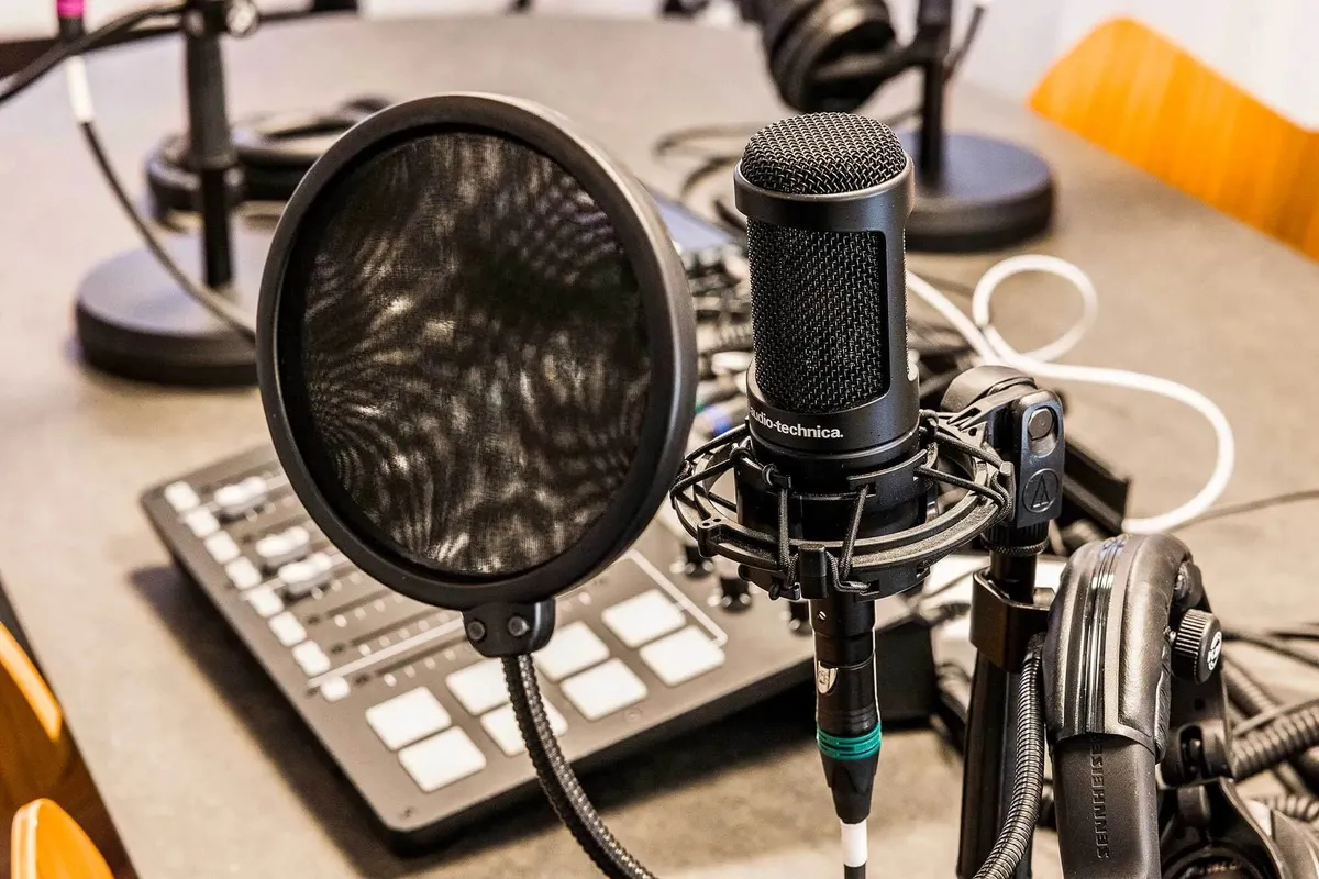 Et mikrofonstativ med en mikrofon og et headset samt en tastatur, kabel og andet kontorudstyr på bordet