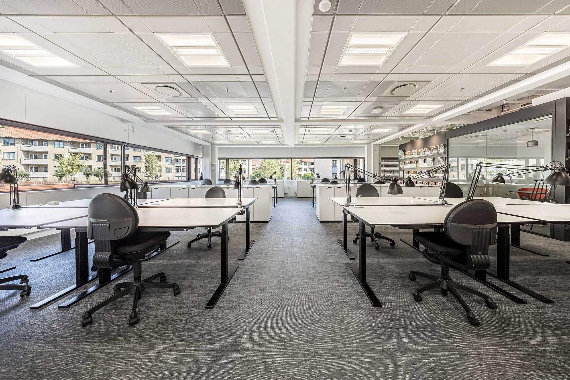 Kontor med lyse lofter og flere skriveborde med stole og lamper i et moderne og funktionelt design