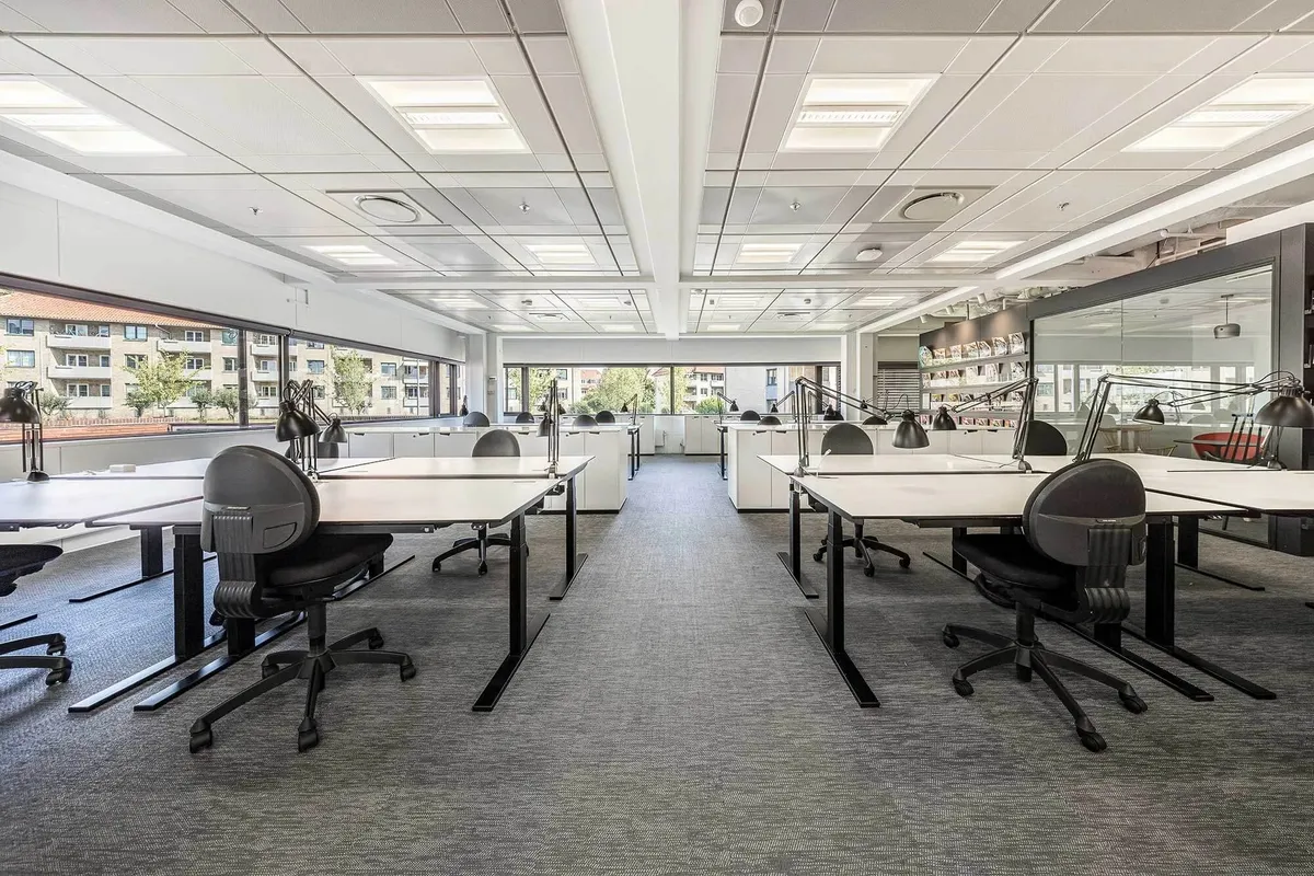 Kontor med lyse lofter og flere skriveborde med stole og lamper i et moderne og funktionelt design