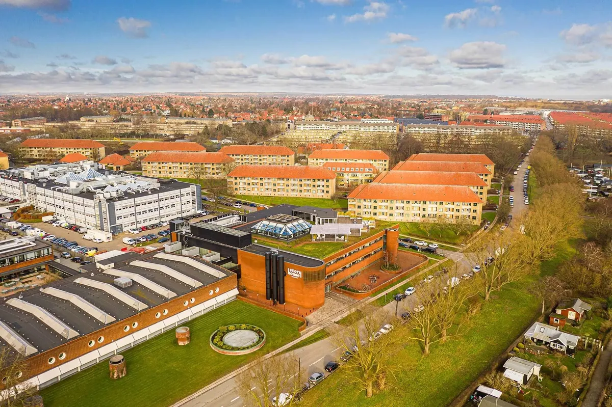 Kontorområder med mange bygninger og biler parkeret foran i et skovområde i solskin