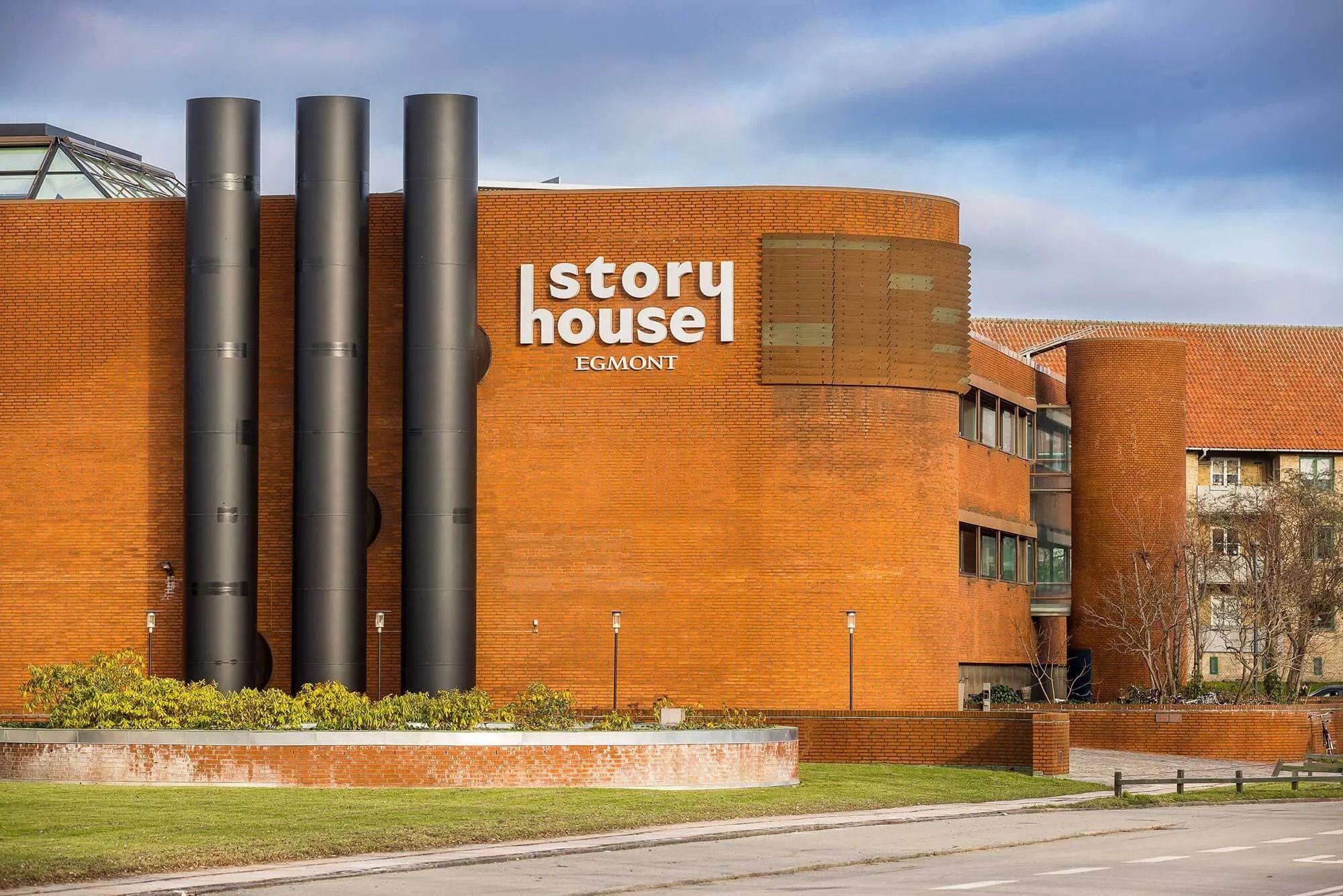 En orange bygning med tre store røgslanger, teksten Story House Egmont og nogle planter foran