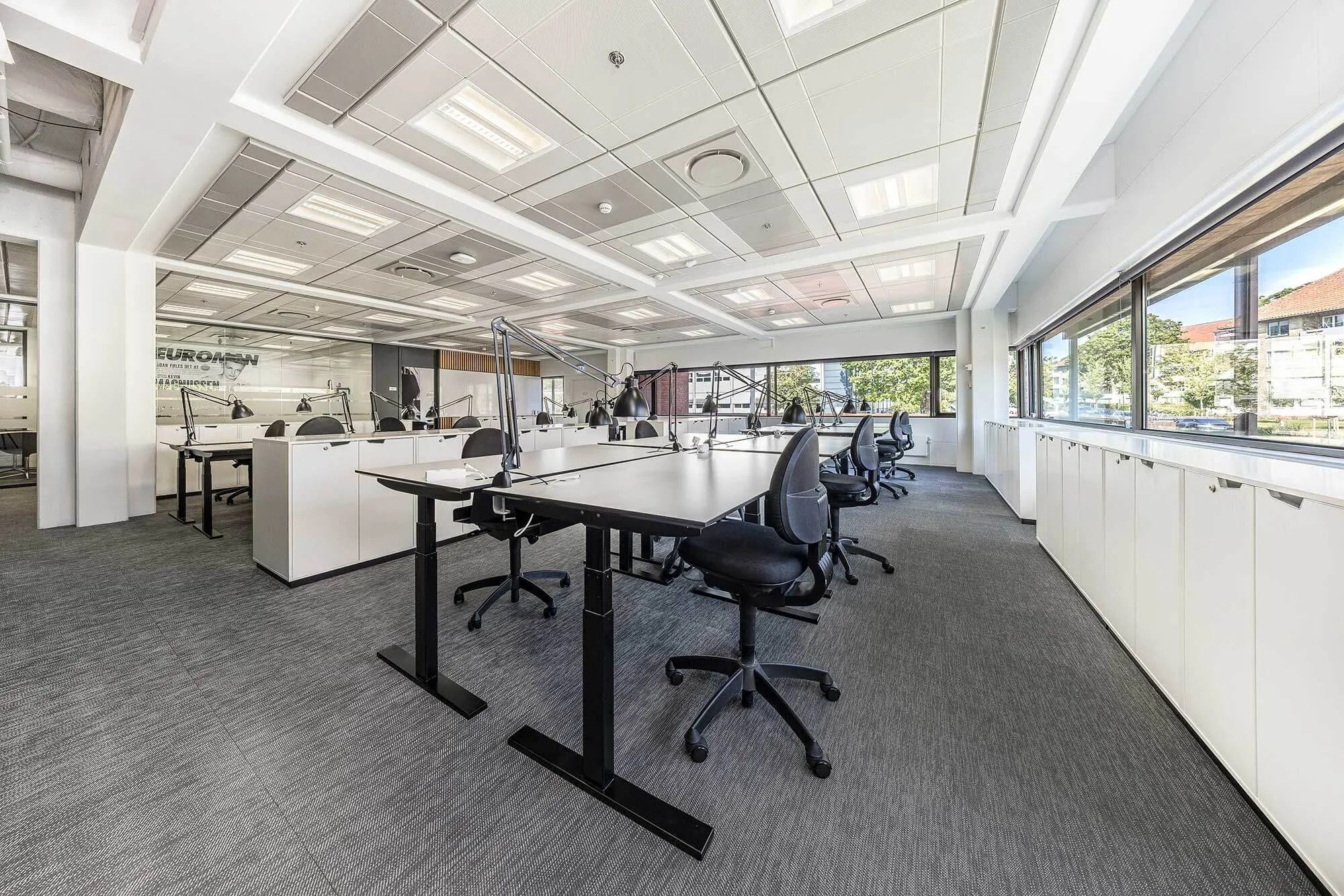En stor og moderne kontorrum med højt gulv og møbler, vinduer og lyse lofter