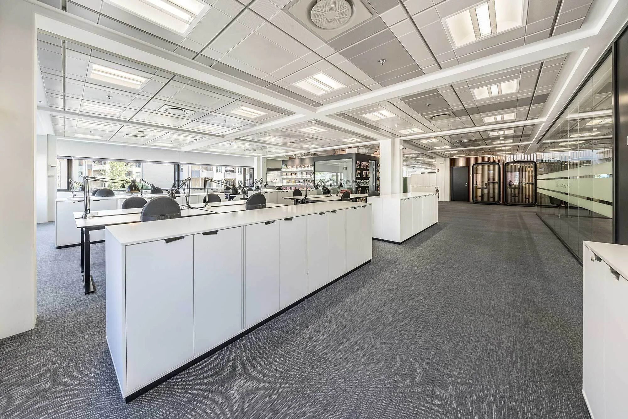 Kontorområde med hvide lofter og gulv, glasvægge og borde med stolpe og lampe