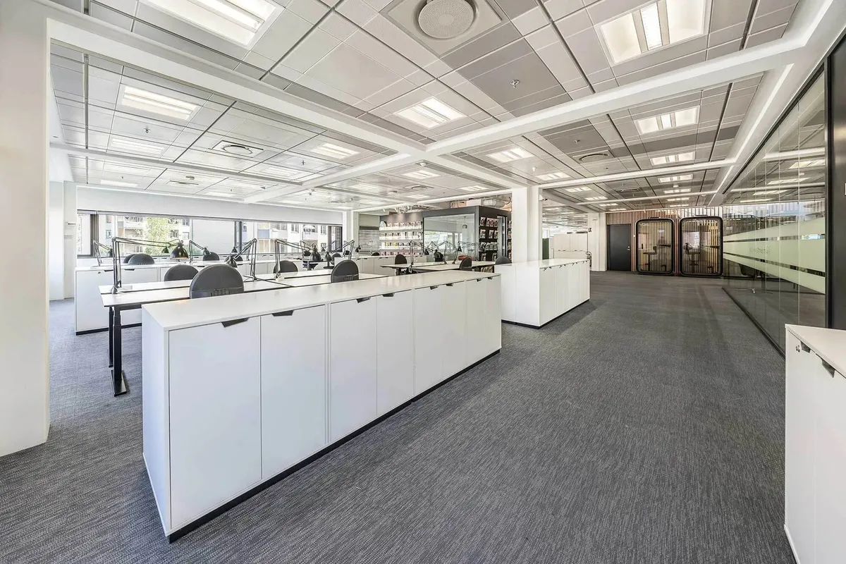 Kontorområde med hvide lofter og gulv, glasvægge og borde med stolpe og lampe