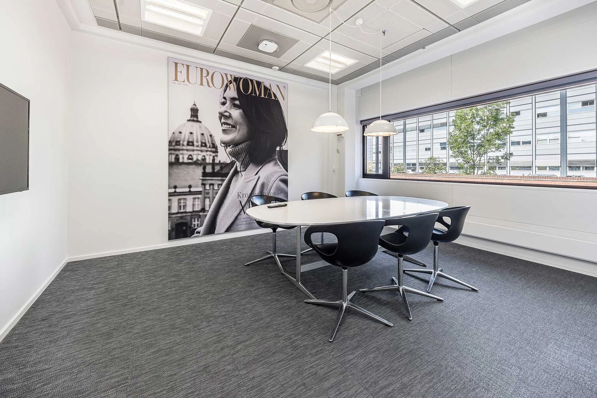 Kontorrum med møbelsæt og stor plakat med en kvinde og teksten Eurowoman