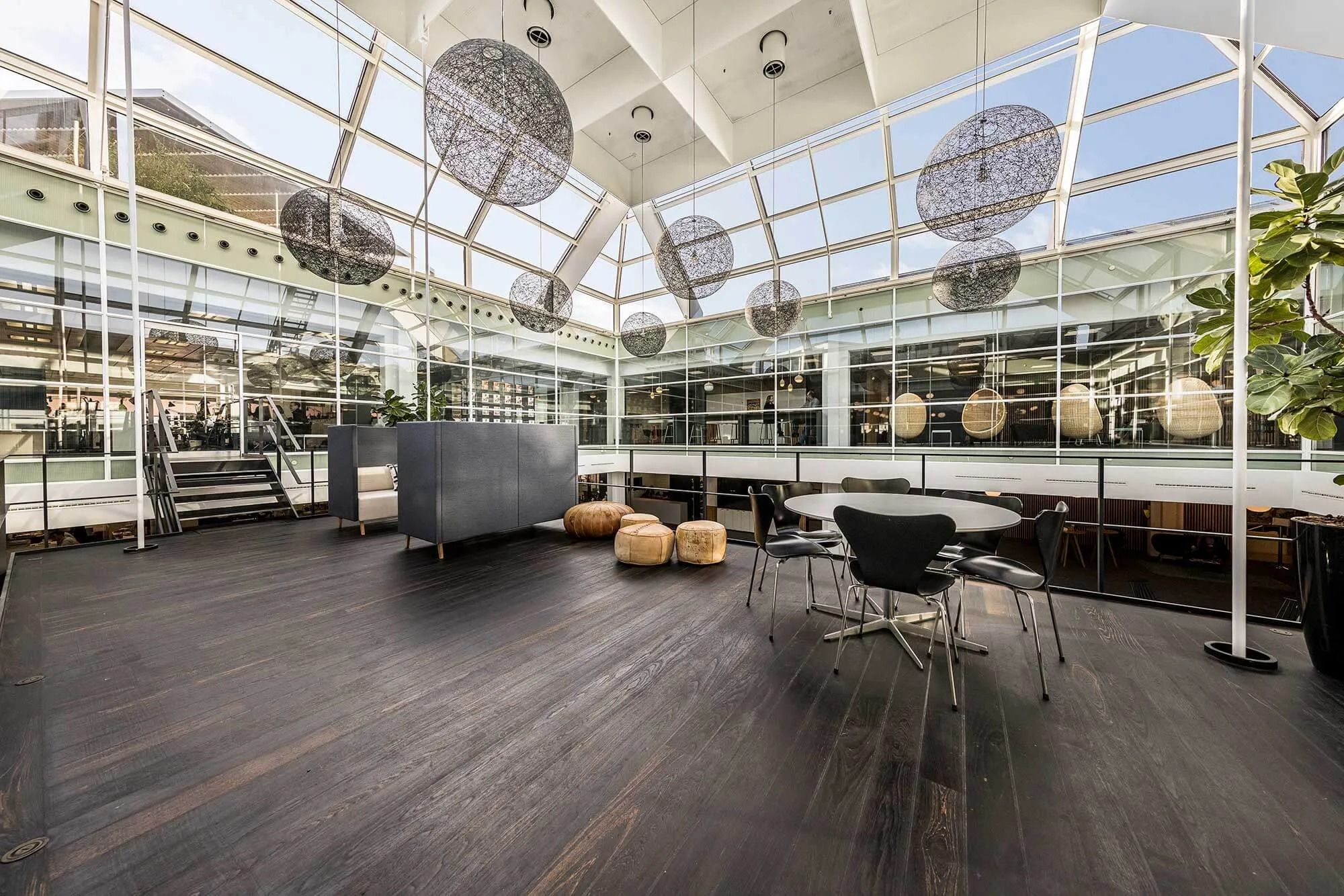 Kontor med højt glasloft, lyse stole, massivt bord, hyggeligt møbelstykke og plante i gryden